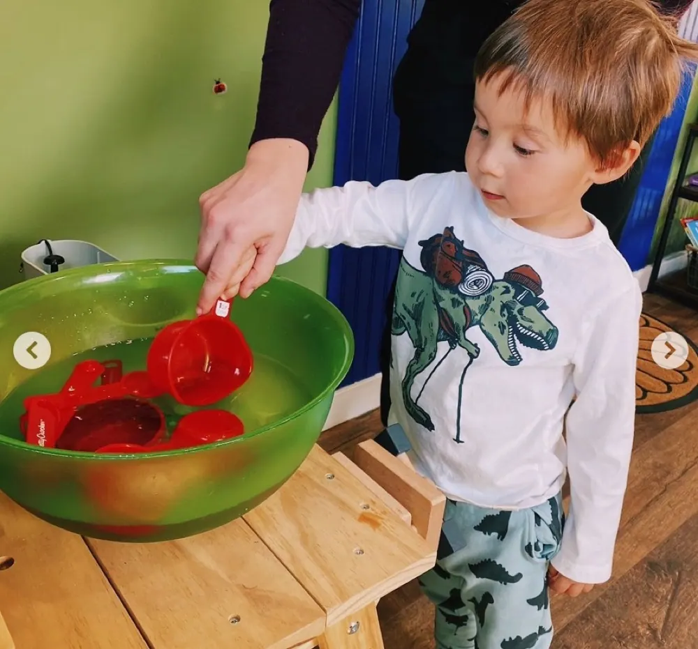 A young child pouring measuring cups in a play activity with a Traina therapist