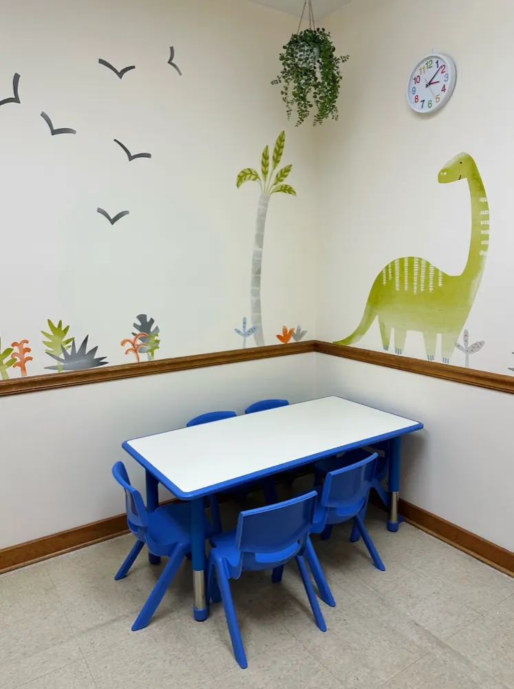 A blue child-sized table in a bright therapy room with a dinosaur mural