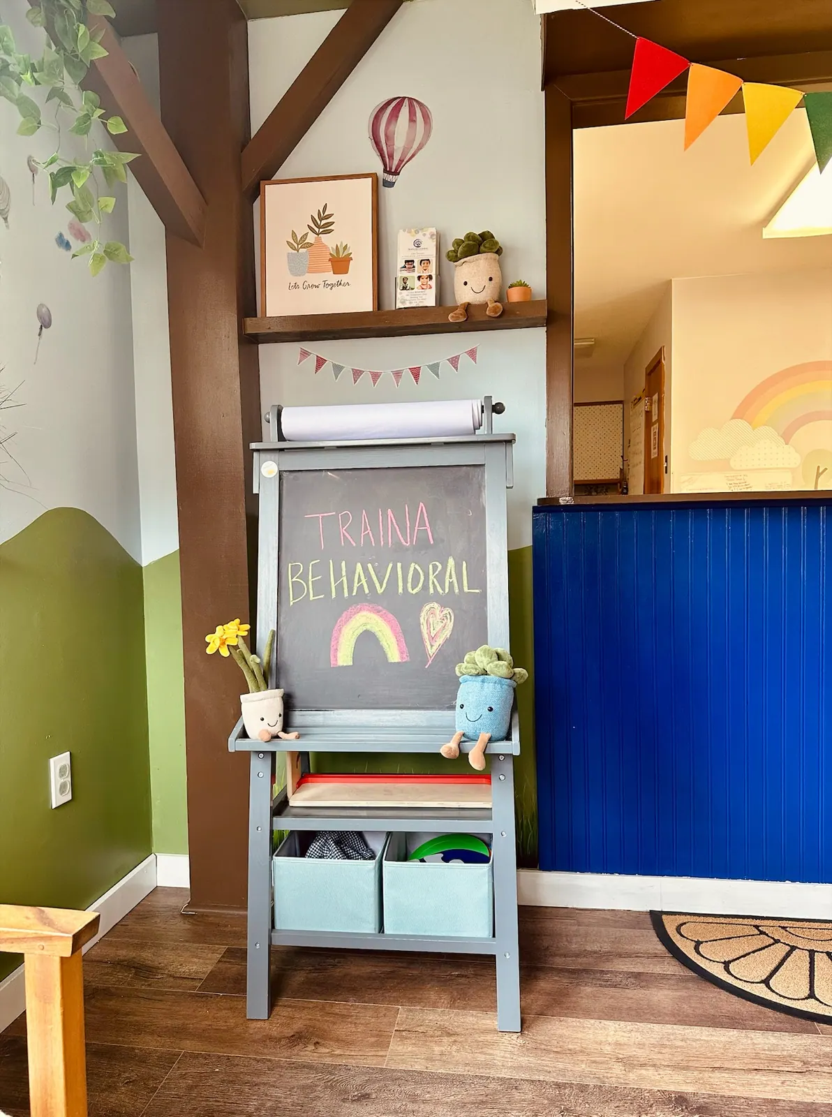 A chalkboard easel reading Traina Behavioral with a chalk rainbow and heart, in the center's entry.