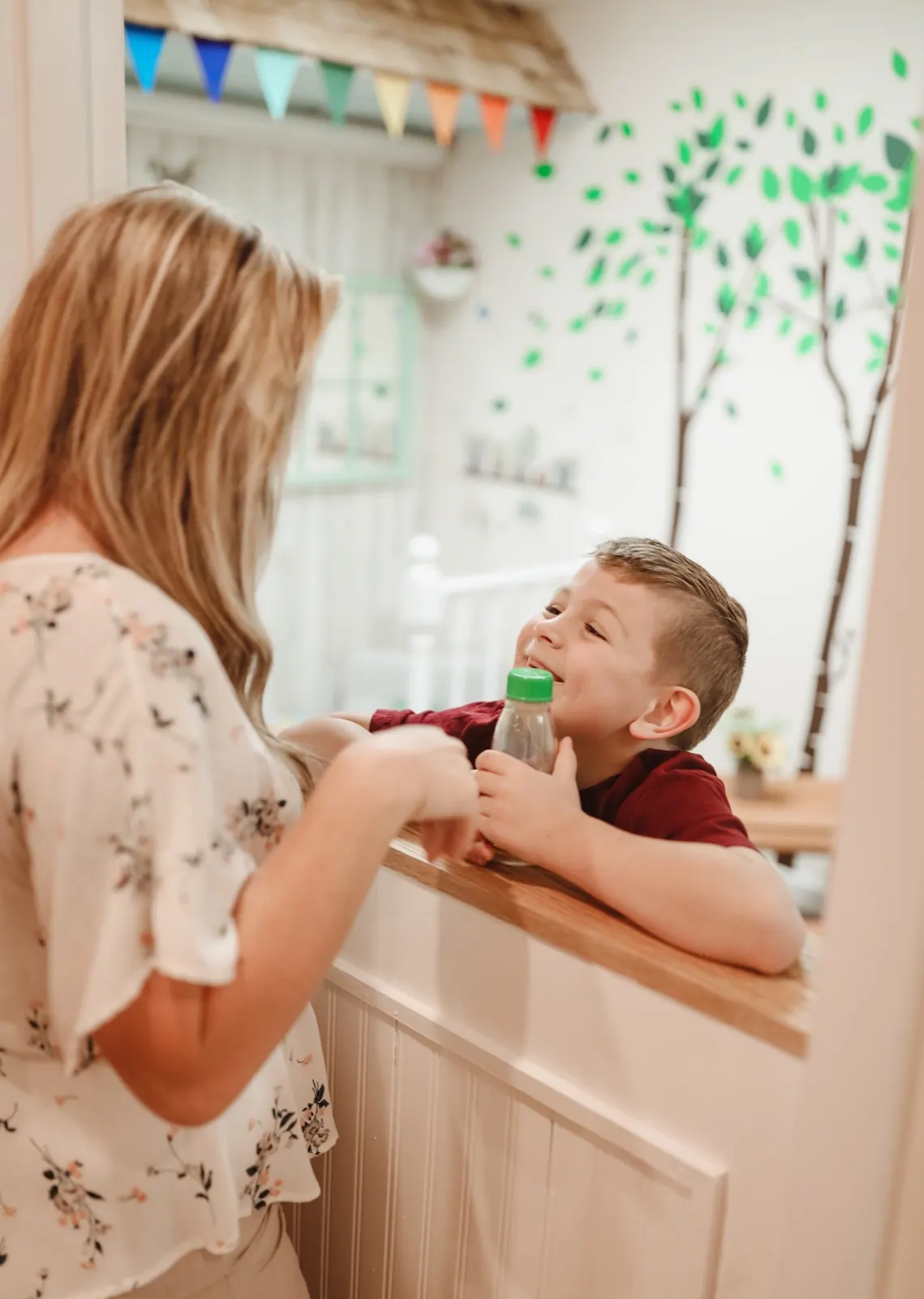 A smiling boy leans on a counter, talking with his therapist.