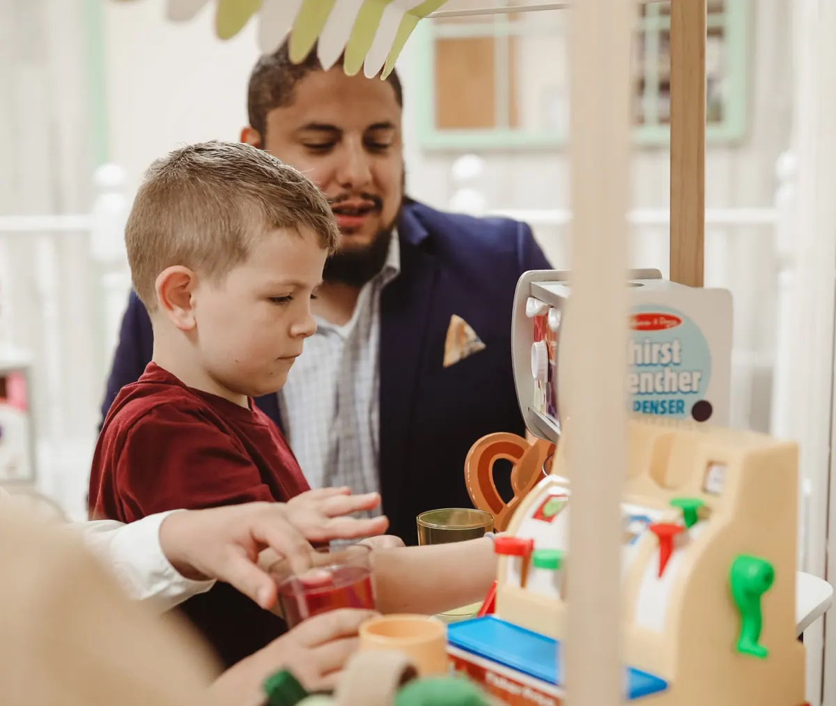 A Traina clinician looks on as a boy plays with a toy cash register and drink dispenser.