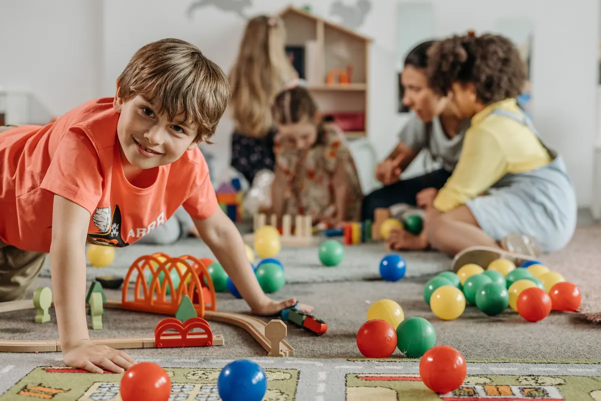A child smiling during group playtime with other children and a caregiver