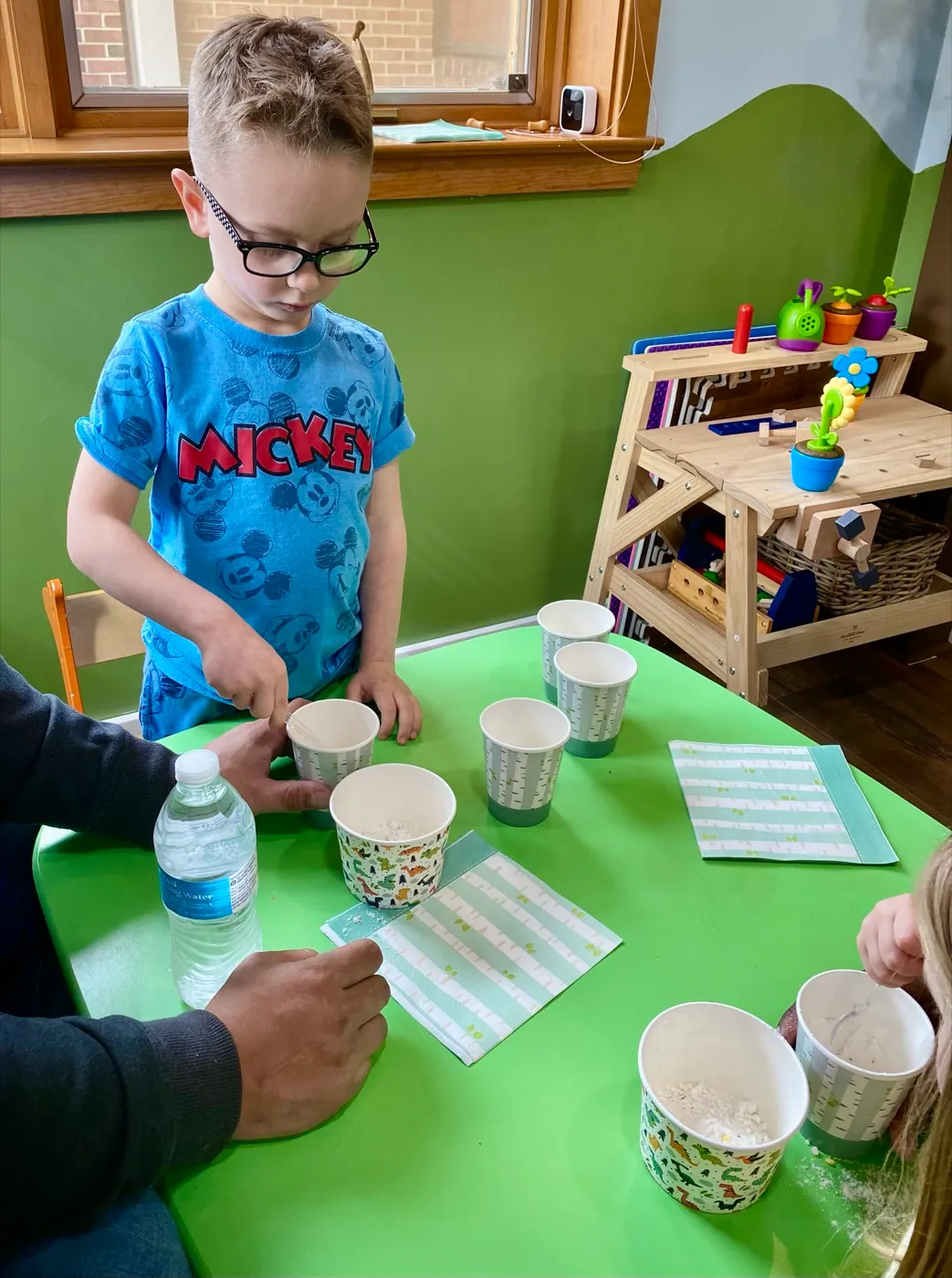 A boy practicing a mealtime-style routine with cups and napkins at a table