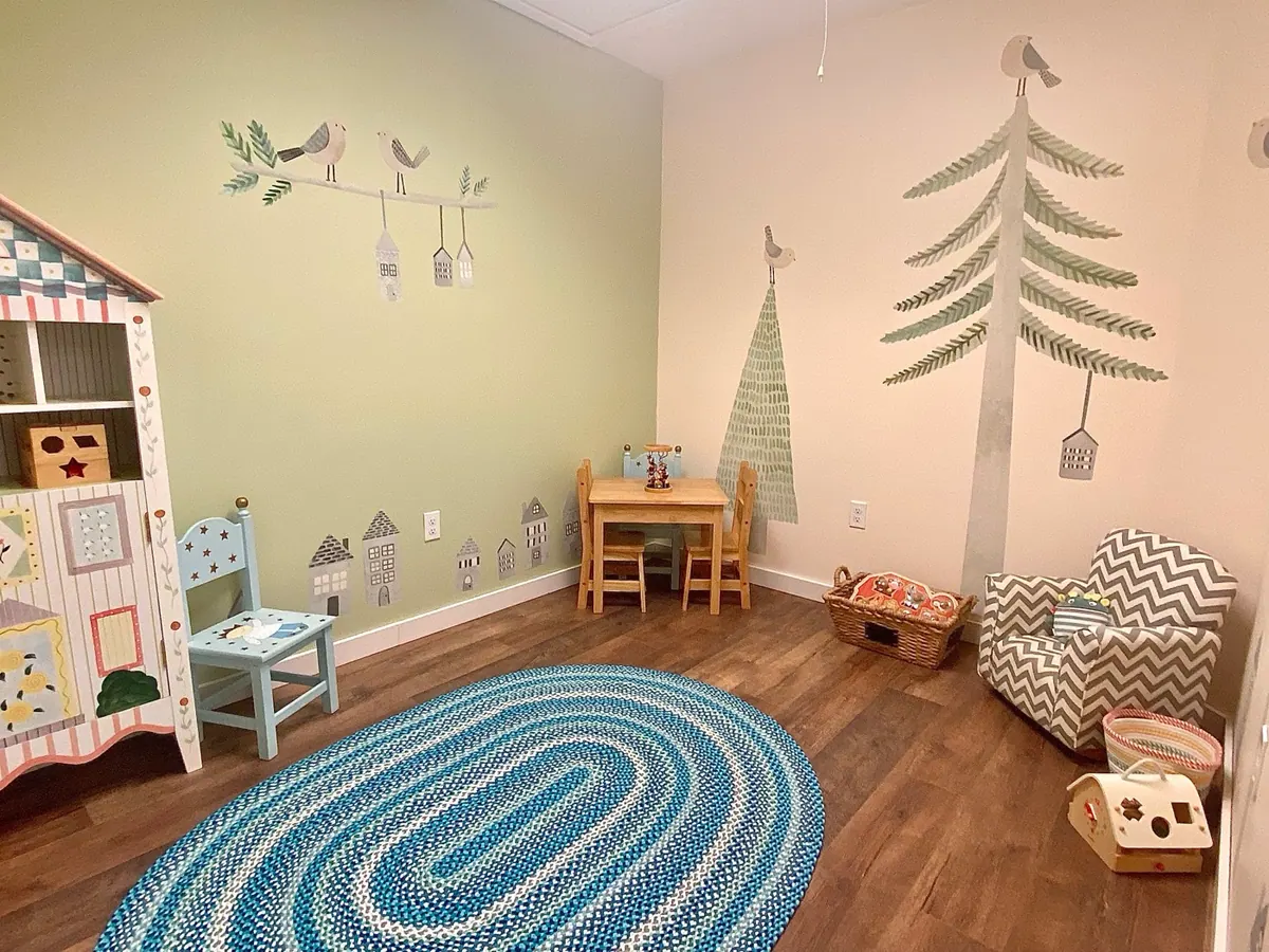A calm, cozy corner of a Traina room with a small table, chairs, and a woodland mural